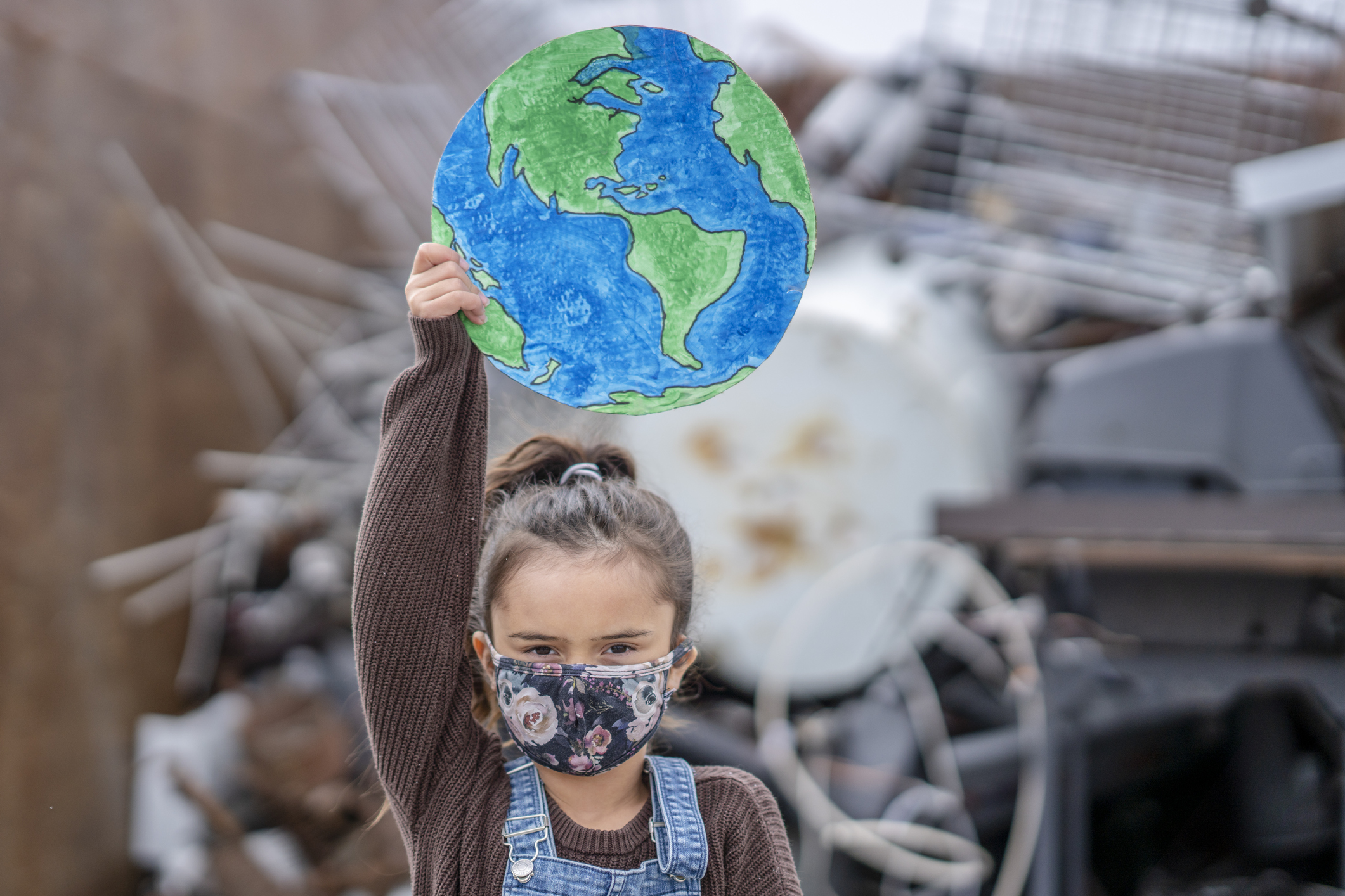 Young child holding picture of Earth with a facemask on.