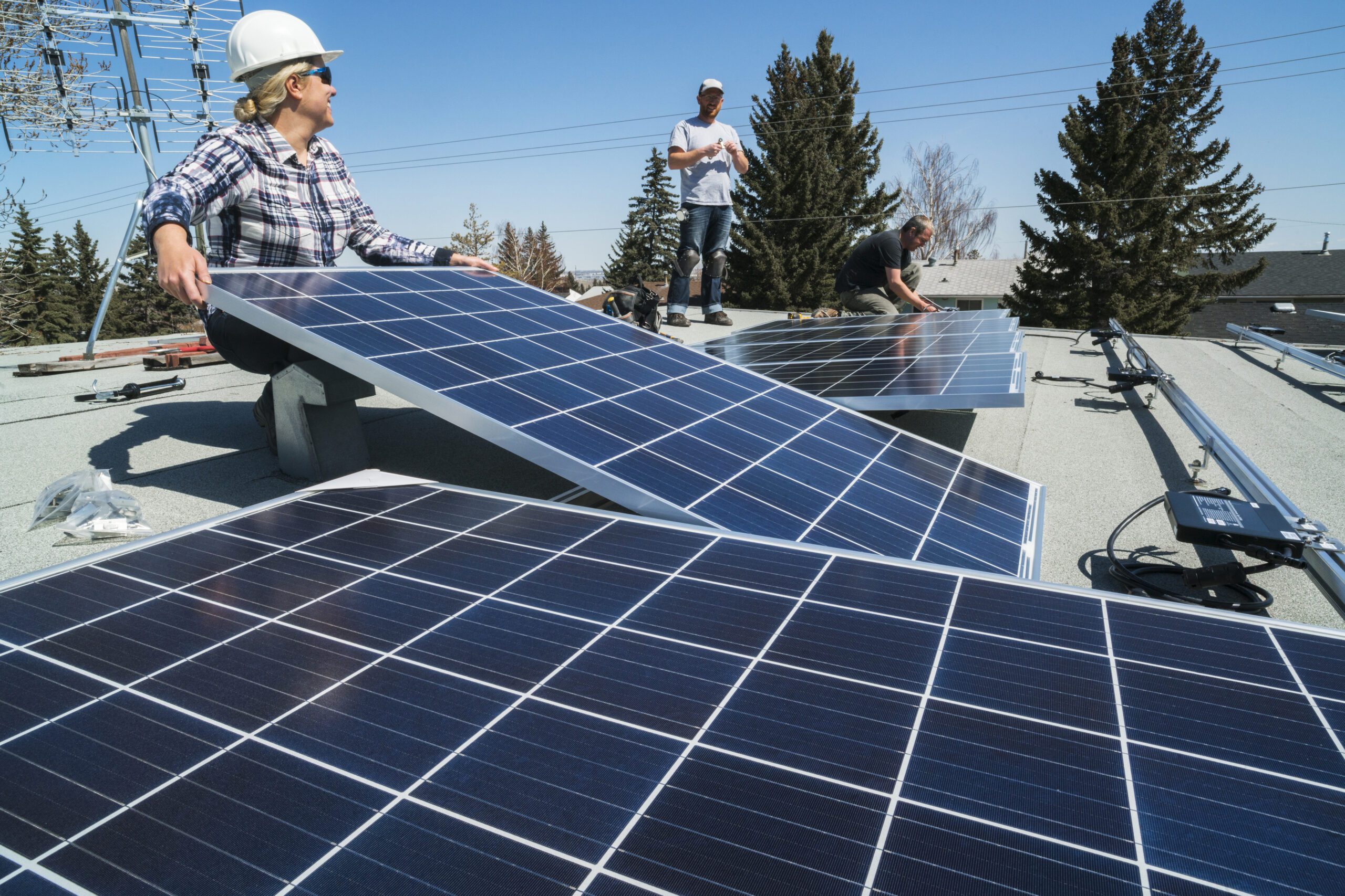 Three people installing solar photovoltaic panels.